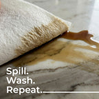 Marble surface with coffee spill and paper towel, text 'Spill. Wash. Repeat.'
